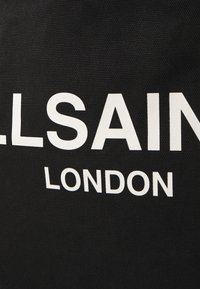 Borsa nera in canvas con testo bianco audace "ALLSAINTS LONDON." Il materiale ha una finitura testurizzata con cuciture visibili.