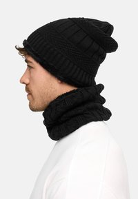 Black knitted beanie and infinity scarf set with ribbed texture. Both items feature a thick, cozy design suitable for cold weather.