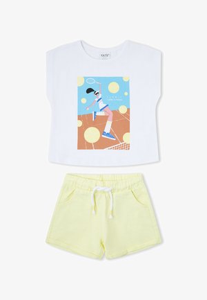 Top blanco sin mangas con gráfico de jugador de tenis combinado con pantalones cortos de tiro elástico y cordón de color amarillo claro.