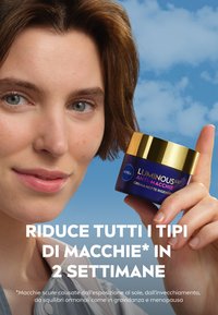 Barattolo di vetro rotondo con base blu navy e coperchio dorato, contrassegnato "NIVEA LUMINOUS 630 ANTI-MACCHIE", tenuto da una persona contro un cielo blu.
