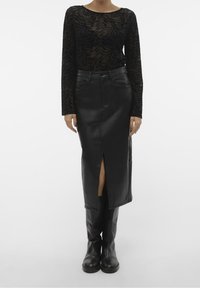 Svart nät långärmad topp med texturerat zebra-mönster, kombinerad med en högmidjad svart läderkjol med en framfåra, bärs med svarta stövlar.