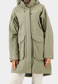 Parka imperméable verte avec capuche, dotée de deux grandes poches devant, de boutons-pression et de poignets élastiques. Texture lisse, longueur aux genoux.