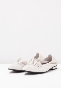 Pantofole bianche in suede con un accento arricciato sulla punta, forma rotonda e un piccolo dettaglio metallico sul tallone.