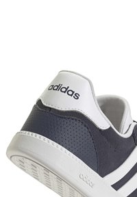 Baskets Adidas avec un dessus texturé gris foncé, des accents blancs et trois bandes. Présente un talon blanc avec le logo Adidas. Semelle à motif circulaire.
