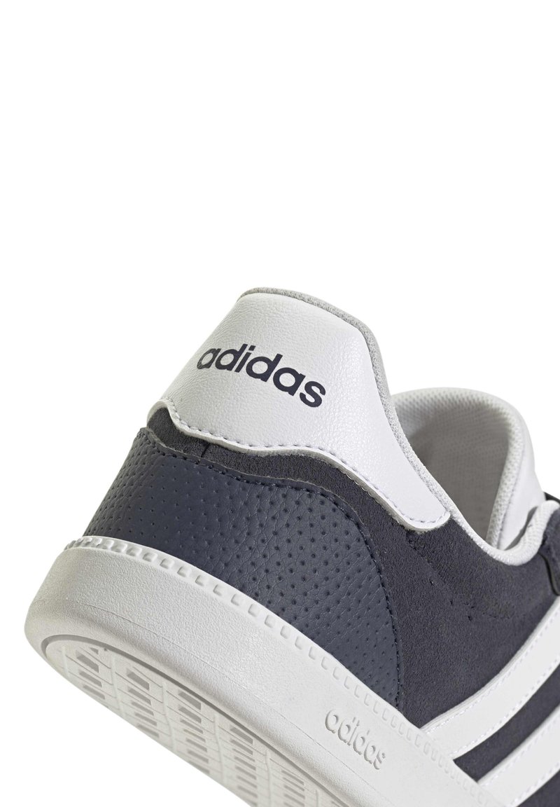 Zapatillas Adidas con una parte superior texturizada en gris oscuro, detalles blancos y tres bandas. Presenta un talón blanco con la marca Adidas. Suela con dibujo circular.