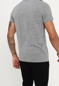 Camiseta gris de manga corta hecha de una tela texturizada, con un diseño ajustado, cuello redondo y costuras visibles.