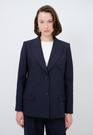 Blazer navy in tessuto strutturato, con rever a prefilo, due bottoni, tasche frontali e un accento triangolare sul petto.
