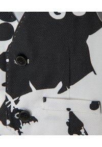 Svartvitt mönstrat tyg med en texturerad yta. Har en enda svart knapp och en liten fickdetalj.