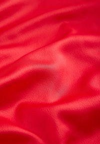 Tissu rouge lisse avec des plis doux et une texture subtile créant des variations de lumière et d'ombre.