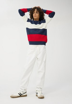 Maglione lavorato a maglia con strisce blu navy, bianche e rosse; abbinato a pantaloni jogger bianchi e sneakers bianche con strisce nere.