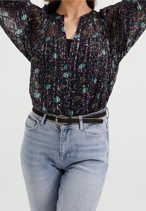 Schwarze durchsichtige Bluse mit buntem Blumenmuster, plissierter Textur und V-Ausschnitt, kombiniert mit hellblauen Jeans und einem schwarzen Gürtel mit silberner Beschläge.