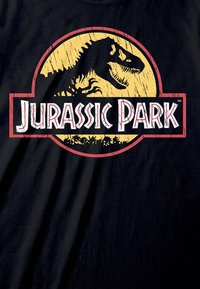 Černé tričko s kulatým, opotřebovaným logem na žlutém pozadí, siluetou dinosaura a textem "Jurassic Park" v bílé a červené barvě.
