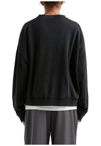Felpa nera con una vestibilità rilassata, polsini e orlo a coste. Realizzata in tessuto morbido con un design minimalista, presenta un'ampia apertura per il collo.