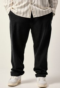 Pantalones de mezclilla negros con un corte relajado, combinados con zapatillas blancas. La tela tiene una textura suave con un ligero estiramiento.