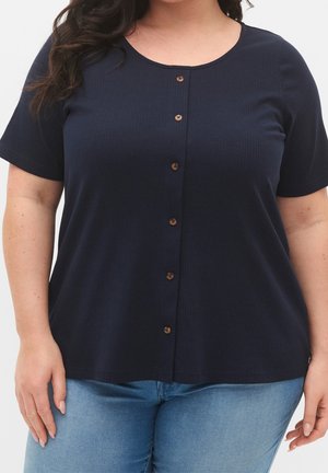 Marineblauwe geribbelde knoopjes T-shirt met korte mouwen, voorzien van houten knopen en een ronde halslijn. Gecombineerd met lichtblauwe denim.