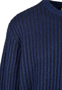 Sotilas Sininen neulepaita, jossa on pystyribbaus, pyöreä pääntie ja pitkät hihat. Materiaali vaikuttaa pehmeältä ja hieman paksulta.