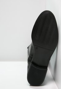 Botte en cuir noir avec une semelle en caoutchouc texturé. Comprend une fermeture éclair et des détails de couture sur le côté. Fini lisse avec un bout arrondi.