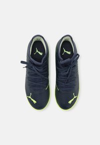 Puma soccer shoes in navy blue and fluorescent yellow. Features textured design, rounded toe, and lace-up closure with logo accents.