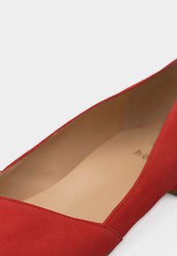 Κόκκινο γυναικείο παπούτσι μπαλέτου με μυτερή μύτη, μαλακή υφή σουέντ και μπεζ εσωτερική επένδυση, γωνιασμένο για να αναδεικνύει την εσωτερική σόλα και τις λεπτομέρειες της ραφής.