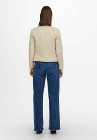 Beige takatu puku me te waist e whai ana, i pootihia ki nga jeans miraka pootu ka mau ki te waewae. Ko te tuitui he maeneene me te hoahoa hanganga.