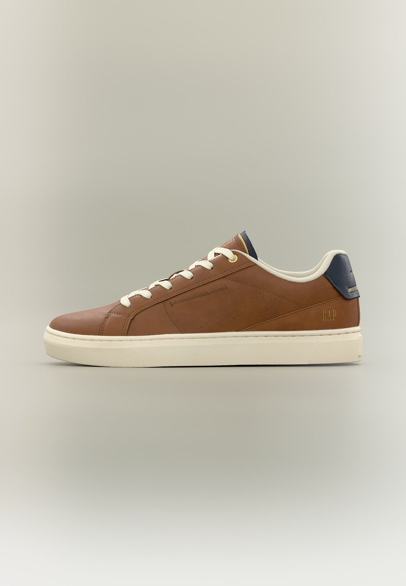 Baskets basses en cuir marron avec lacets blancs, semelle blanche et languette de talon bleu marine, vue de profil sur un fond neutre.