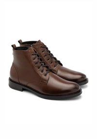 Brązowe skórzane botki za kostkę o gładkim wykończeniu, z sześcioma oczkami, czarnymi sznurowadłami i solidną czarną gumową podeszwą.