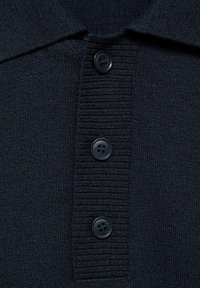 Gros plan sur un tissu tricoté bleu marine foncé avec trois gros boutons noirs en rangée verticale le long d'une patte côtelée.