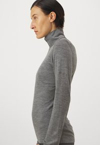 Svetlý šedý rolák s dlhým rukávom vyrobený z mäkkej, textúrovanej látky. Má vysoký golier a elegantný, priliehavý strih s minimalistickým brandingom.