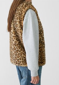 Leopardenmuster-Faux-Fur-Weste mit weicher Textur, darunter ein graues Langarmshirt und blaue Jeans. Seitenansicht dargestellt.