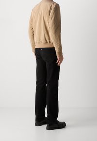 Beige bomberjacka med ribbat nederkant, tillsammans med svarta raka jeans och svarta skor. Stilen är avslappnad och modern.