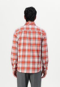 Camicia in flanella a quadri rossi e bianchi con maniche lunghe e polsini a bottoni, caratterizzata da un colletto classico e un dettaglio sulla spalla posteriore.