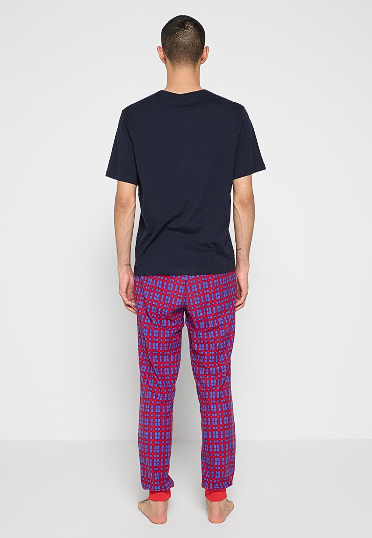 Camiseta navy de manga corta combinada con pantalones de pijama en cuadros rojos y azules, con puños rojos acanalados. Vista trasera, fondo liso.