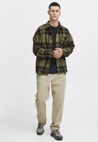 Groen en zwart geruit flanellen overhemd over een zwart T-shirt, gecombineerd met beige broeken en grijze wandelschoenen met zwarte accenten.