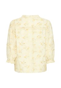 Blouse jaune clair à manches longues avec un petit motif floral orange, détails plissés au dos et aux poignets, et un col doux.