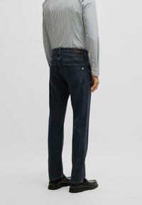 Mörkblå denimjeans för män med slim-fit, med distinkta bakfickor, logopatch och en mjuk yta. Stylar med en randig skjorta.