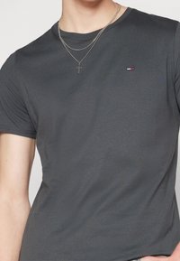 Graues Baumwoll-T-Shirt mit rundem Halsausschnitt und kurzen Ärmeln. Besitzt ein kleines, rot, weiß und blau gesticktes Logo auf der Brust.