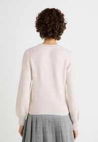 Maglione rosa chiaro con colletto rotondo, maniche lunghe, polsini e orlo a costine, realizzato in materiale morbido. Abbinato a una gonna a quadretti grigia.