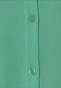 Grüner Textilstoff mit vertikalen Linien; verfügt über einen runden Knopf mit vier Löchern an der Knopfleiste. Weiches und leichtes Material.