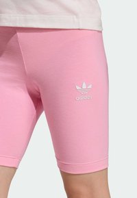 Ružové športové šortky z pružnej tkaniny s bielym logom Adidas a priliehavým strihom končiacim tesne nad kolenami.