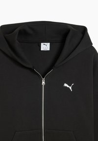 Felpa nera con zip realizzata in tessuto morbido, dotata di tasca a marsupio, cappuccio regolabile con coulisse e logo Puma bianco sulla parte sinistra del petto.