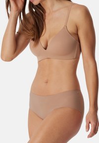 Beige rintaliivi syvällä v-aukkolla ja säädettävillä olkaimilla, yhdistettynä saumattomiin beigeihin bikineihin. Pehmeä pinta ja minimalistinen muotoilu.