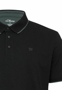 Schwarzes Polohemd mit strukturiertem Finish, ausgestattet mit einem grünen Kragenbündchen und drei schwarzen Knöpfen. Logo auf der linken Brustseite angebracht.