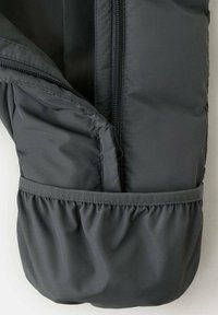 Sección de chaqueta acolchada gris con abertura con cremallera y dobladillo elástico, con una textura suave y detalle de tela fruncida.