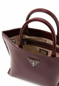 Sac à main en cuir marron avec deux poignées supérieures, une forme structurée et un accent triangle avec logo. L'intérieur comprend une poche zippée et une doublure de marque.