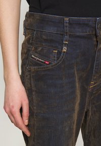Donker denim jeans met een vervaagd patroon, contrasterende gele stiksels en een merketiket op de voorzak. Heeft een rechte snit.