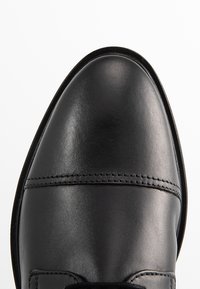 Scarpa da dress in pelle nera con punta arrotondata, texture liscia e un sottile dettagli di cucitura nella parte superiore. La suola è elegante e minimalista.