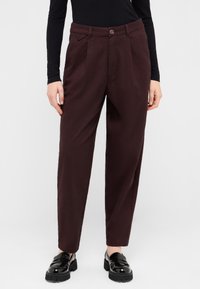 Burgundy tailored trousers with a textured finish, featuring side pleats, a front button closure, and a regular fit. Paired with black shoes.