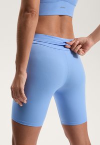 Svetlo modri visokorasli kolesarski šortji iz raztegljivega materiala, z gladko teksturo in tesno prileganje. Logotip je viden na pasu.