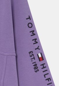Fioletowa bluza z haftowanym napisem i logo "TOMMY HILFIGER" z niebieskimi, białymi i czerwonymi akcentami, wykonana z miękkiego materiału.