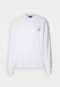 Sweatshirt blanc à manches longues avec col rond, poignets côtelés, petit visage souriant brodé en bleu sur la poitrine gauche, et étiquette HUGO à l'intérieur du col.